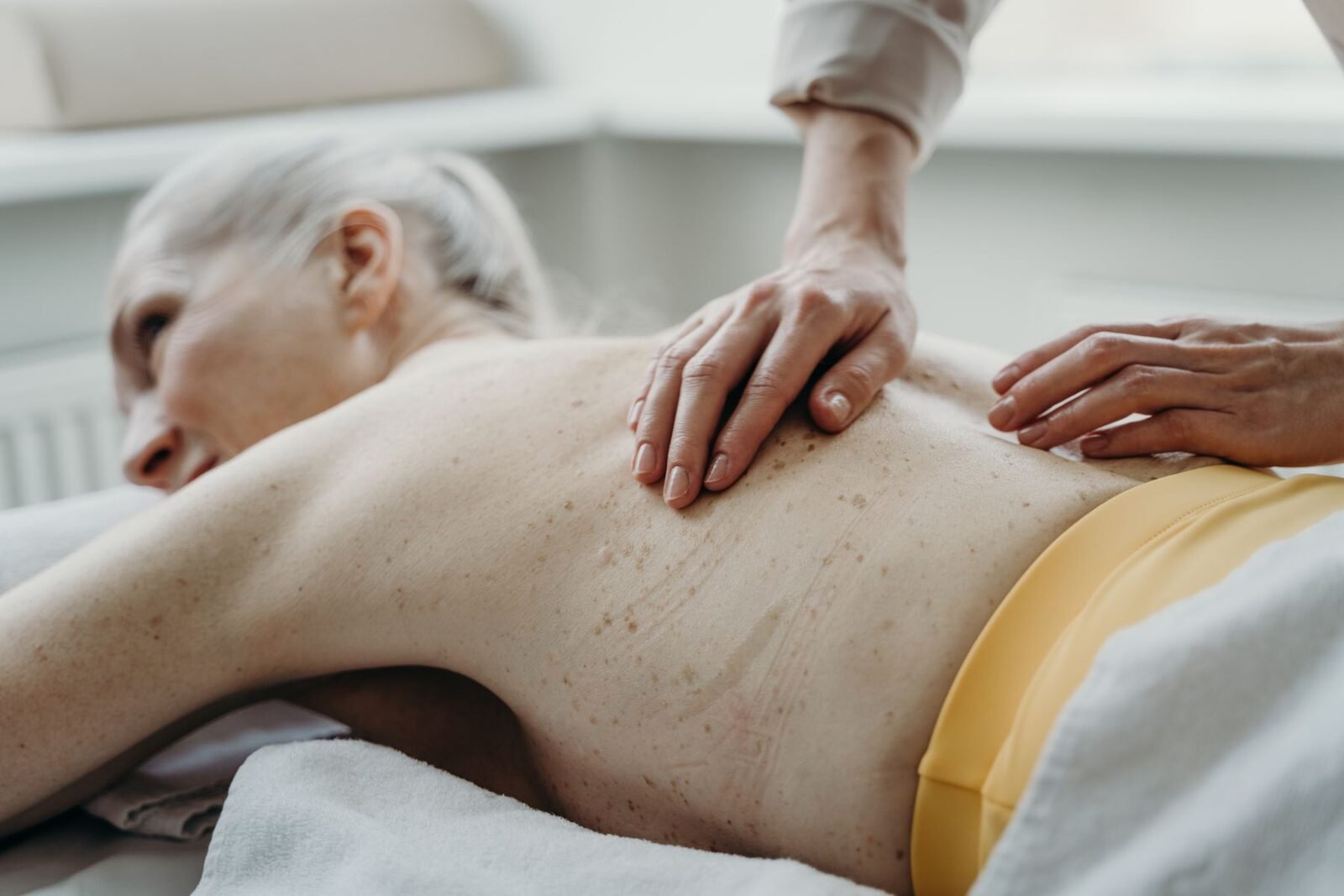 Handen van een fysiotherapeut masseren de rug van een oudere vrouw